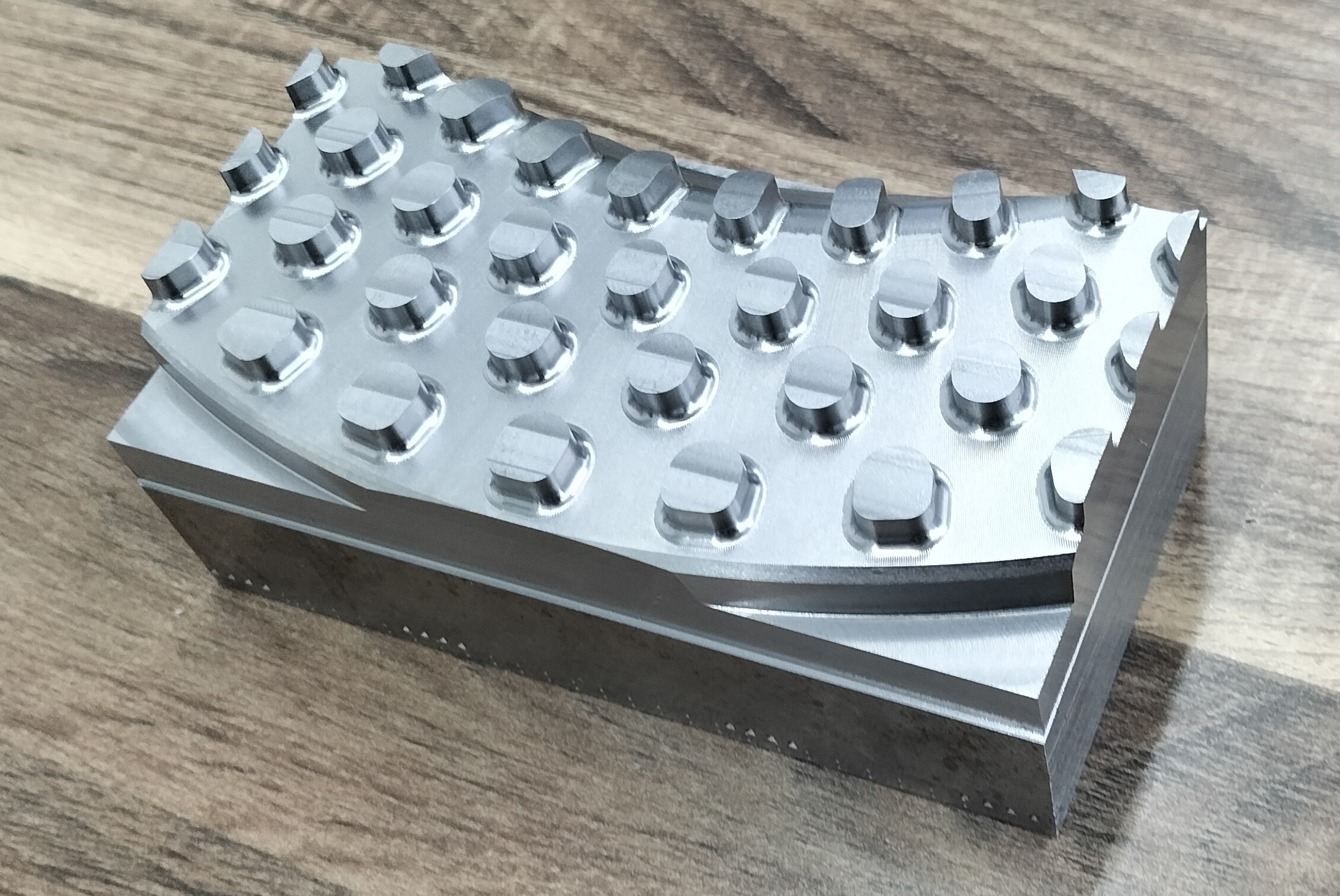 Fertig gefrästes Bauteil, sauber bearbeitet und auf einem Holztisch drapiert. Das Bauteil zeigt eine makellose Oberflächenqualität und präzise Verarbeitung.