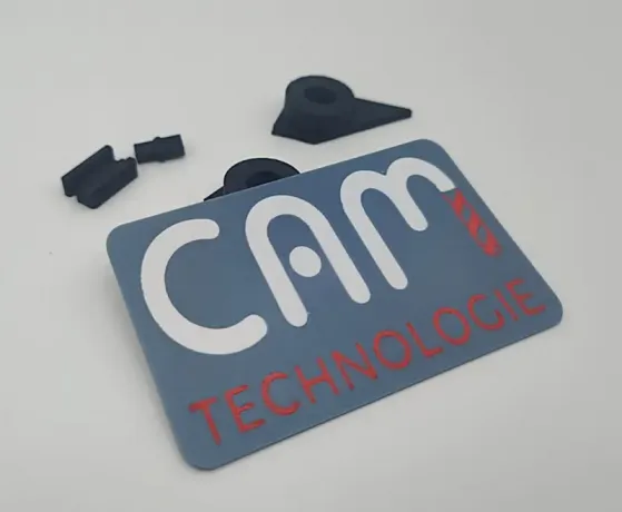 Technisch anmutende, 3D-gedruckte Visitenkarte in Grau, Weiß und Rot, präzise gefertigt. Im Hintergrund vier kleine ABS-Teile aus dem Prototypenbau, die die Vielseitigkeit des 3D-Drucks zeigen.